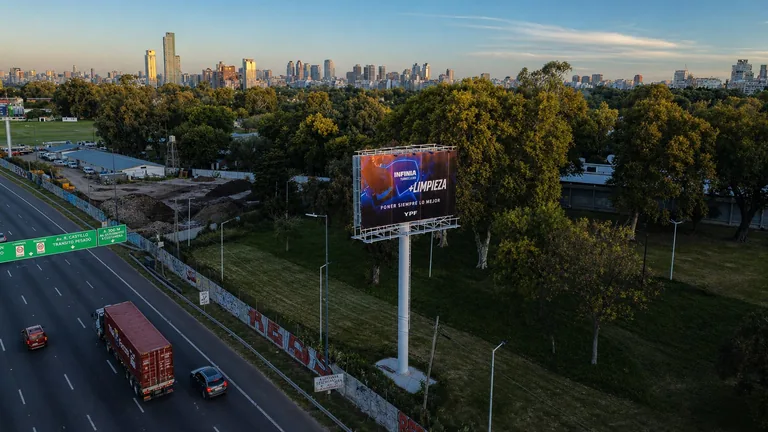 Vista aérea del cartel de YPF INFINIA sobre Av. Lugones, con la Ciudad de fondo